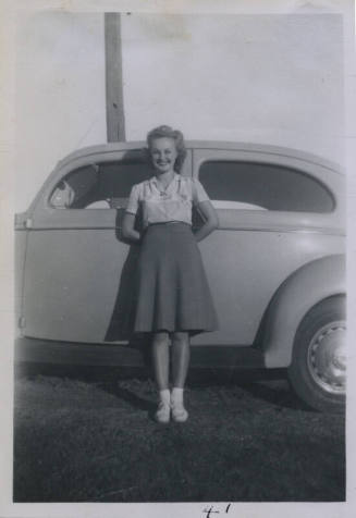 Untitled [Woman leans on car, arms behind her back]