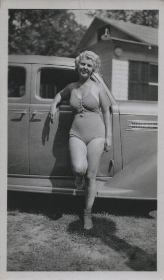 Untitled [Woman in bathing suit and striped socks leans on passenger's seat window, props one leg on car]