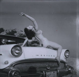Untitled [Woman leans back naked on hood of car, hand points to the sky]
