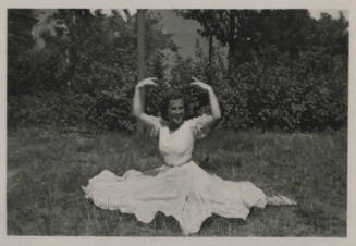 Untitled [Woman sits on garden, hands and arms held up, palms down]