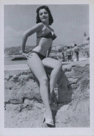 Untitled [Woman in bathing suit sits on beach ledge, hand on her hip]
