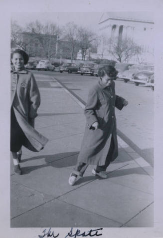 Untitled [Two women stand on curb, perhaps dancing, parking lot in background]