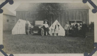 Untitled [Three women, three men, and two children stand in front of two cars and two tents]