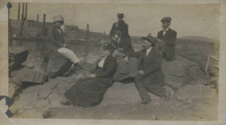 Untitled [Two women and four men sit on rocks, body of water in background]