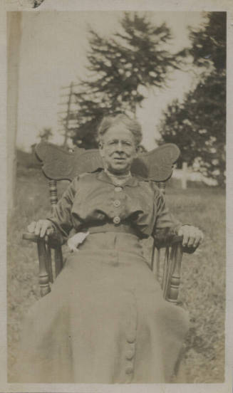 Untitled [Woman sits on chair, in lawn]