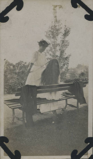 Untitled [Woman sits on bench, woman that stands holds a strand of her hair]