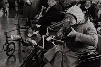 Woman with camera in pull wagon, Lourdes