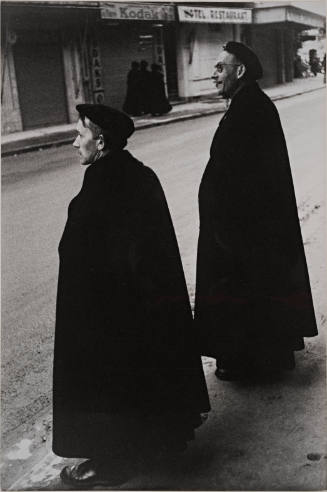 Two men with black hats and capes in profile, Lourdes