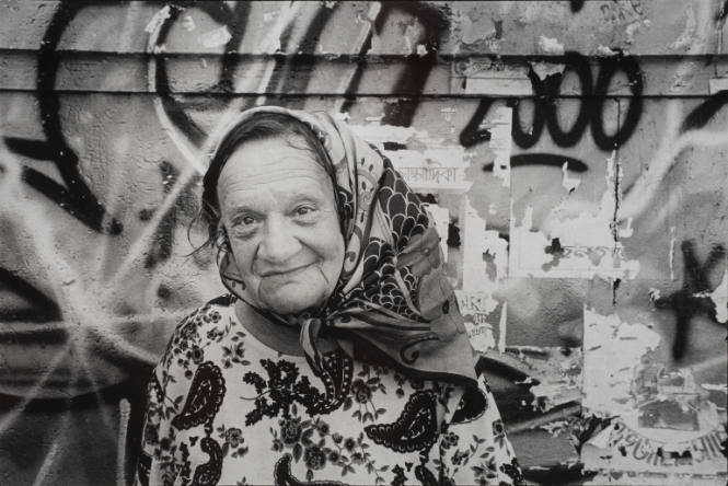 Elderly woman in headscarf against graffiti, Rome, Italy