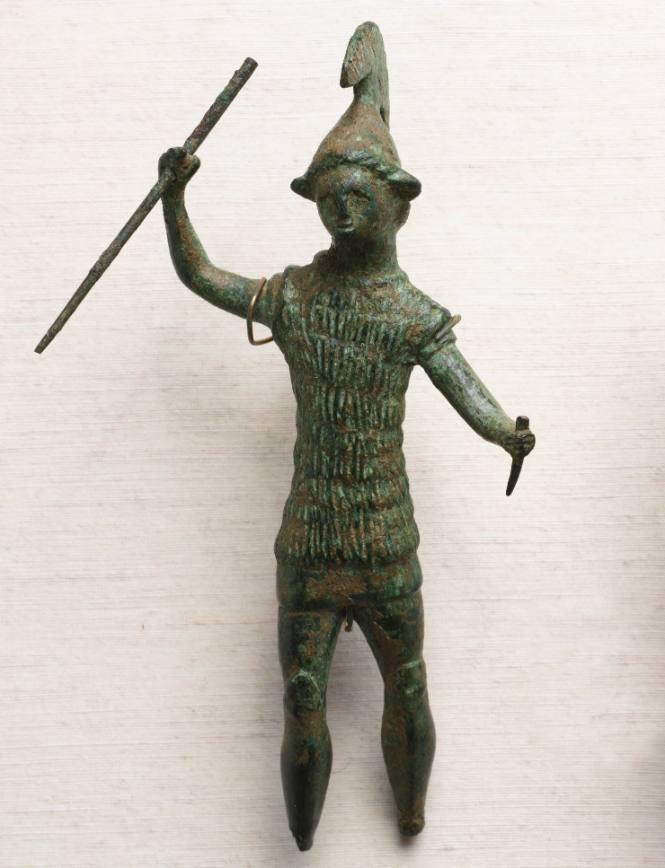 Warrior wearing incised fur cuirass over tunic, crested helmet, with spear in upraised right hand and dagger in left hand