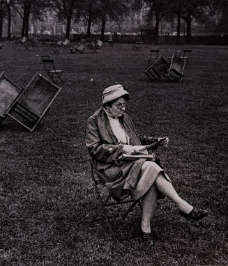 Woman seated in folding chair reading, overturned chairs on grass, England