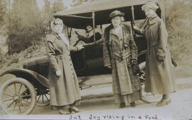 Untitled [Woman sits in car, three women stand on street, all in winter coats and hats]
