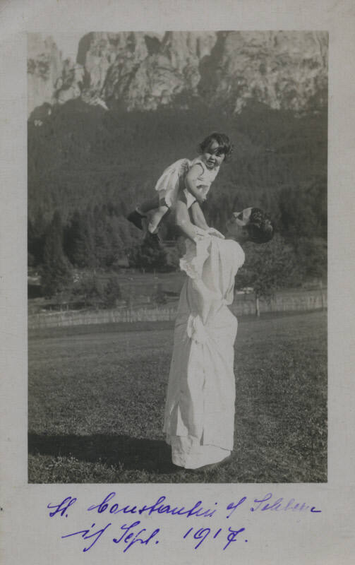 Untitled [Woman in white gown holds up child in mountain setting]