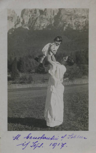 Untitled [Woman in white gown holds up child in mountain setting]