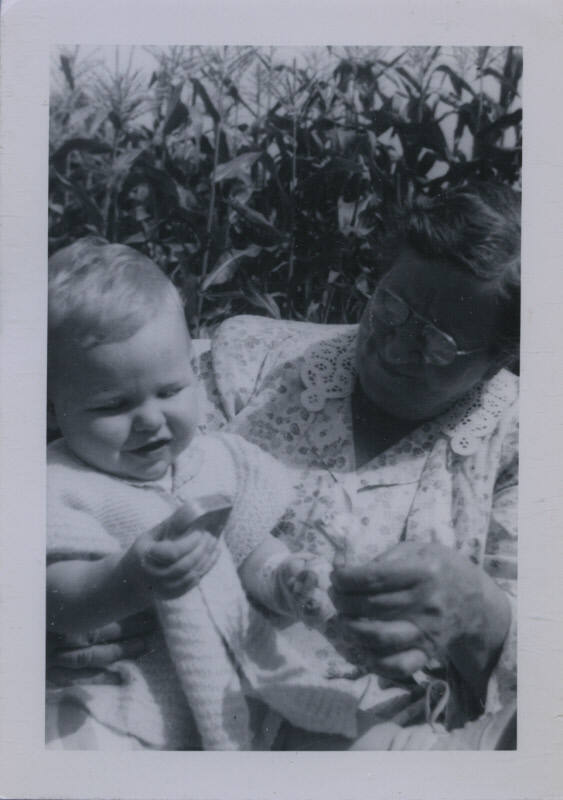 Untitled [Child and woman interact in corn field, woman holds up something for child to see]