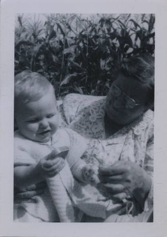 Untitled [Child and woman interact in corn field, woman holds up something for child to see]