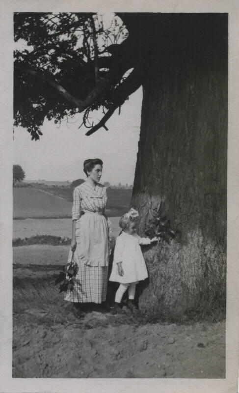Untitled [Woman and child stand by tree and hold branches with leaves]