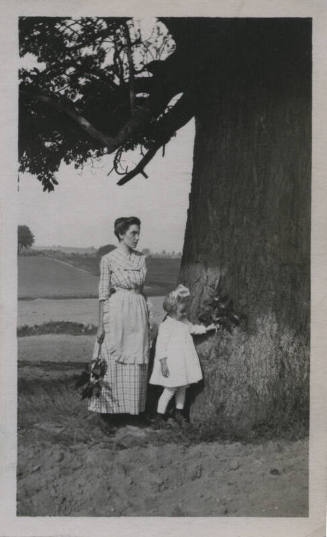 Untitled [Woman and child stand by tree and hold branches with leaves]
