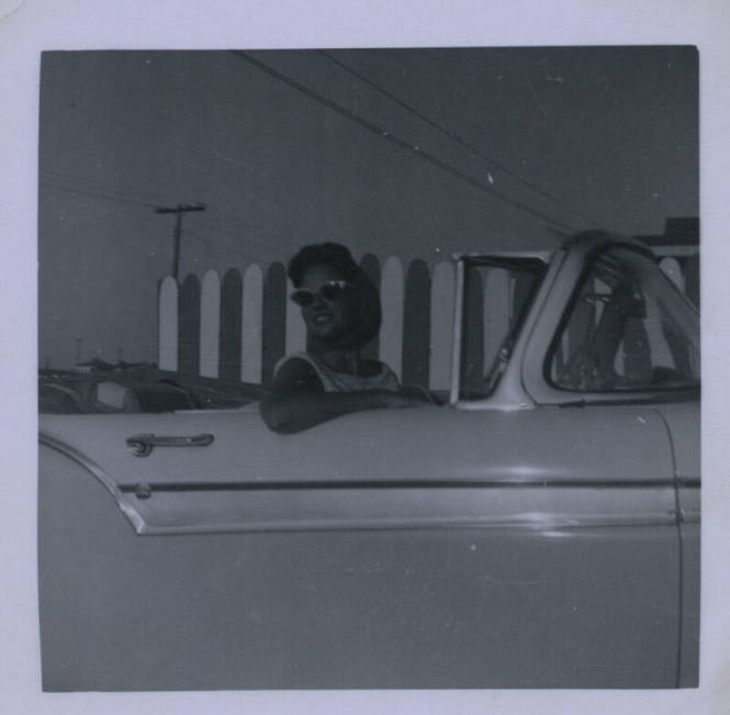 Untitled [Woman with glasses on convertible looks behind her right shoulder from passenger seat]