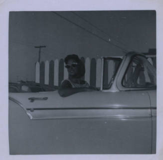 Untitled [Woman with glasses on convertible looks behind her right shoulder from passenger seat]