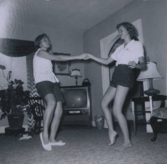 Untitled [Two women in light shirts and dark shorts dance holding each other's hand]