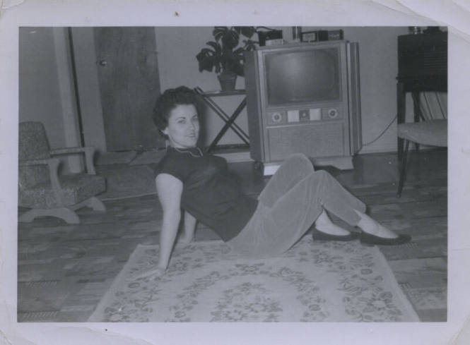 Untitled [Woman sits on carpet, leans back (television and plants in the background)]