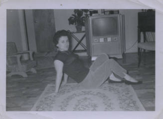 Untitled [Woman sits on carpet, leans back (television and plants in the background)]