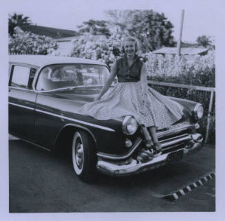 Untitled [Woman sits on car's hood, her patterned skirt spread out]