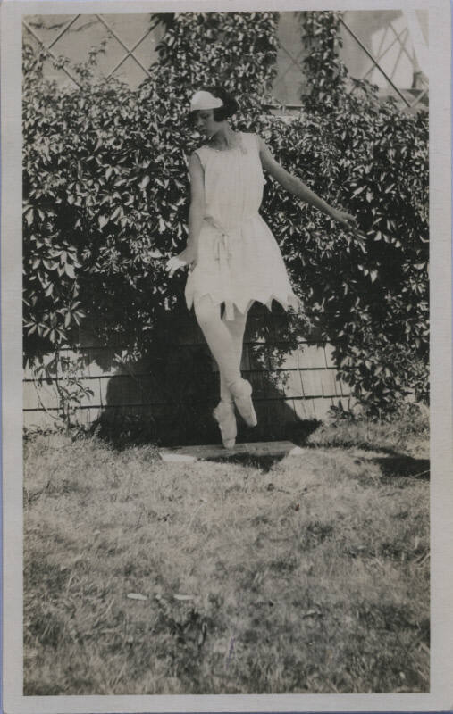Untitled [Woman in pointe shoes and white gown stands in garden]