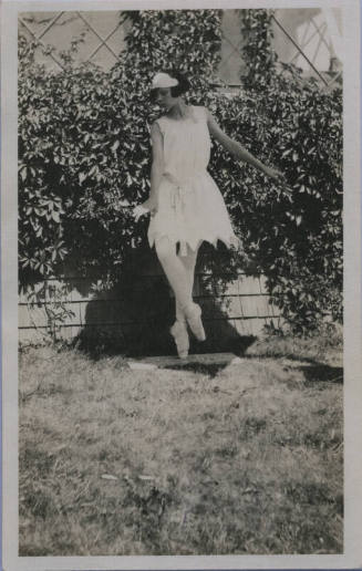 Untitled [Woman in pointe shoes and white gown stands in garden]