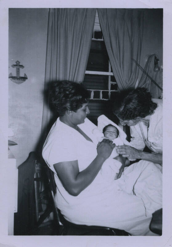 Untitled [Woman holds child on lap, someone leans in, both adults have one hand on child]