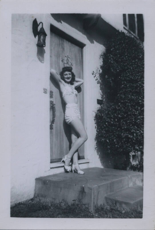 Untitled [Woman in bathing suit stands in doorway, arms raised and hands behind her head]
