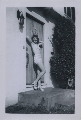 Untitled [Woman in bathing suit stands in doorway, arms raised and hands behind her head]