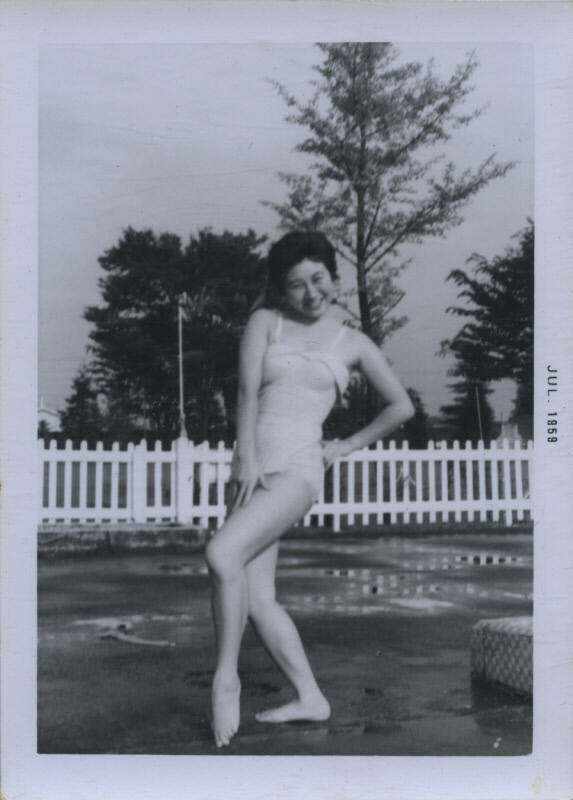 Untitled [Woman in bathing suit props hand on hip, picket fence in the background]