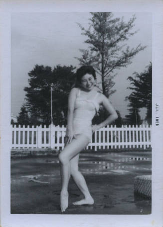 Untitled [Woman in bathing suit props hand on hip, picket fence in the background]