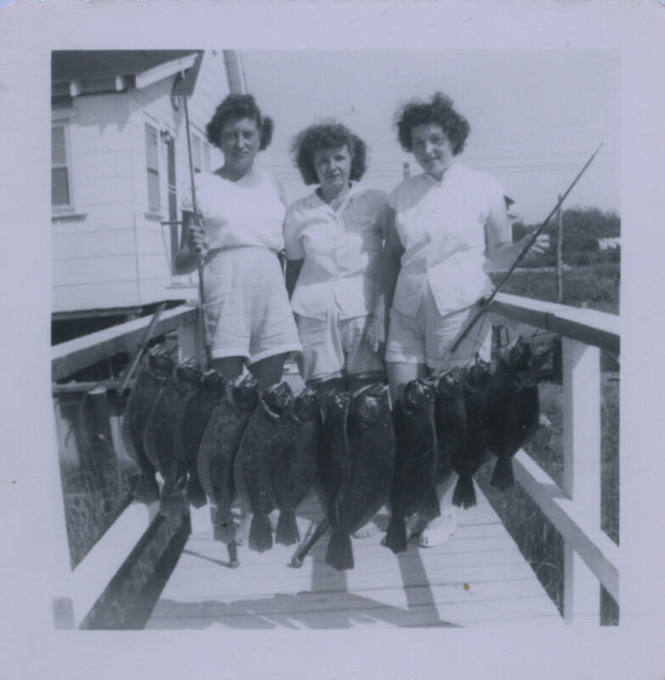 Untitled [Three women on a dock hold up a line of fish]