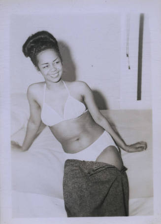 Untitled [Woman sits on bed, leans to one side]