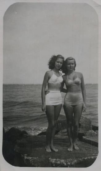 Untitled [Two women in bathing suits stand on a rock, the ocean in the background]