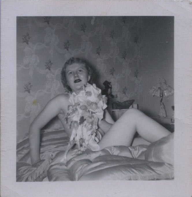 Untitled [Woman lies on bed seemingly naked, holds flowers up to her chest]
