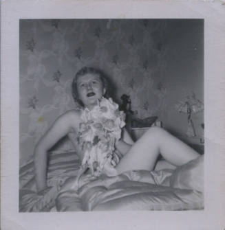 Untitled [Woman lies on bed seemingly naked, holds flowers up to her chest]