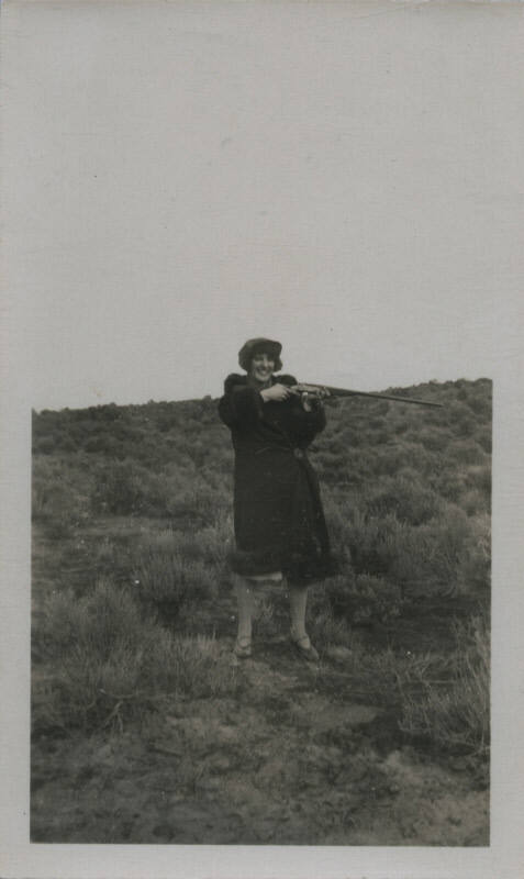 Untitled [Woman on field holds up rifle to one side]