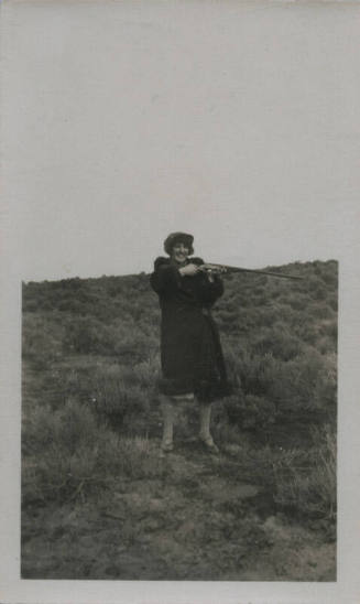 Untitled [Woman on field holds up rifle to one side]