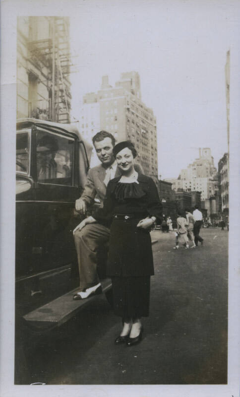 Untitled [Woman and man stand next to car in street]