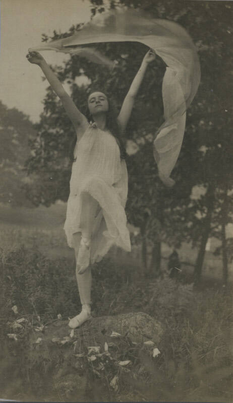 Untitled [Woman in ballet shoes, tights, and dress holds up gauze above head with both hands]