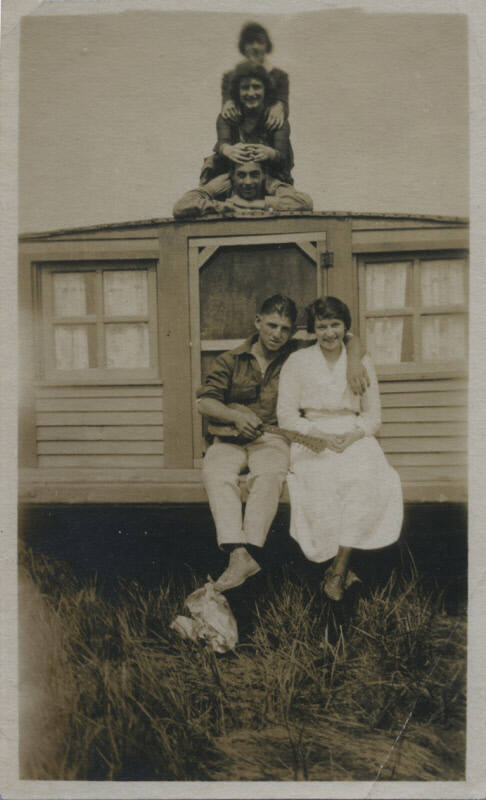 Untitled [Three people pose one on top of another atop house, woman and man sit on bottom edge, man holds guitar]