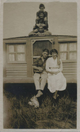 Untitled [Three people pose one on top of another atop house, woman and man sit on bottom edge, man holds guitar]