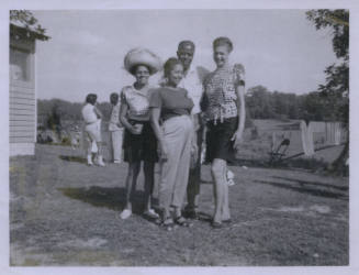 Untitled [Four people stand on a lawn, three people in the back row, one person in front]