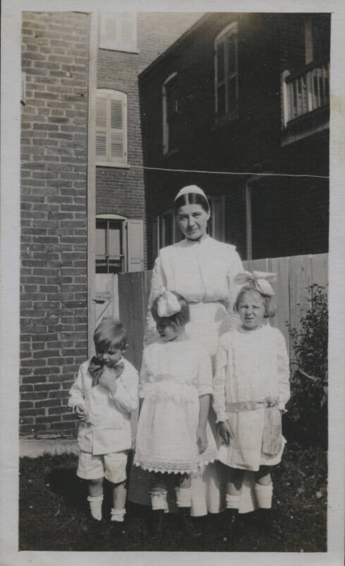 Untitled [Woman stands on lawn, three children in front of her]