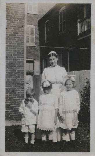 Untitled [Woman stands on lawn, three children in front of her]