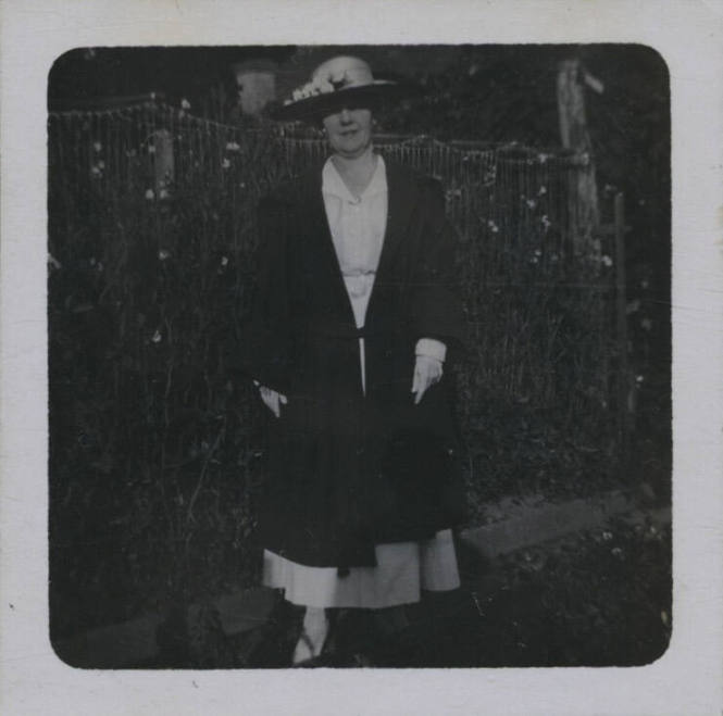 Untitled [Woman wearing hat stands in front of garden fence]